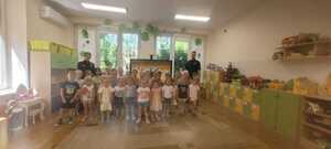 Policjanci stoją razem z przedszkolakami w klasie w trakcie pogadanki.