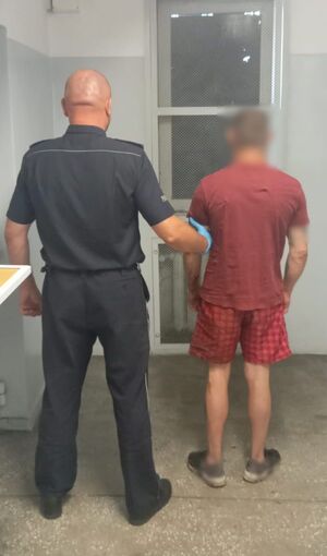 Policjant prowadzi zatrzymanego w pomieszczeniu dla osób zatrzymanych.