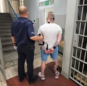 Policjant prowadzi zatrzymanego po korytarzu w budynku komendy.
