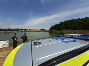 Dach radiowozu, dwaj policjanci oraz w tle zbiornik wodny.
