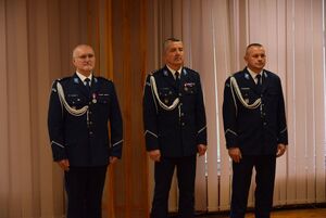 Sala odpraw wieluńskiej jednostki Policji, w sali stoją Zastępca Komendanta Wojewódzkiego Policji w Łodzi, Komendant Powiatowy Policji w Wieluniu, I Zastępca Komendanta Powiatowego Policji w Wieluniu.