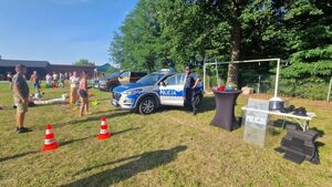 Piknik w plenerze,radiowóz przy którym stoi policjant, rozstawione pachołki.