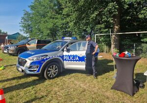 Piknik w plenerze,radiowóz przy którym stoi policjant, rozstawione pachołki.