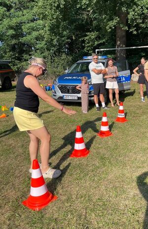 Radiowóz, kobieta w alkogoglach przechodzi pomiędzy rozstawionymi pachołkami.
