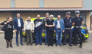Podopieczni Domu Pomocy Społecznej w Skrzynnie wspólnie z dwoma policjantami na tle radiowozu pozują do zdjęcia.