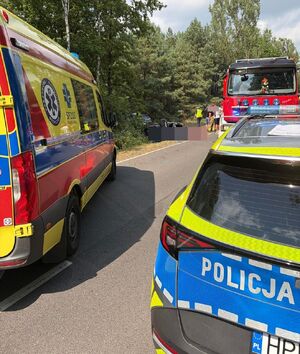 Miejsce zdarzenia, droga, częściowo widoczny radiowóz, karetka wóz strażacki, rozbity samochód oraz policjanci.