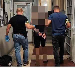 Policjanci prowadzą zatrzymanego po korytarzu w budynku komendy.