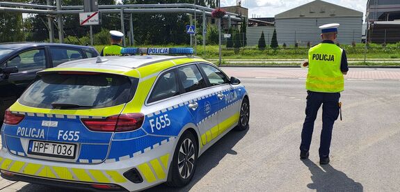 Radiowóz stoi przy drodze, przy nim policjanci.