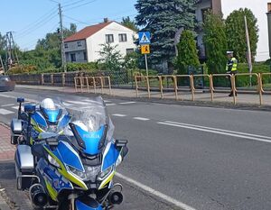 Motocykl, droga przy szkole, przejście dla pieszych przy którym stoi policjant.