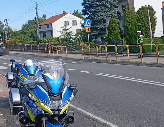 Motocykl, droga przy szkole, przejście dla pieszych przy którym stoi policjant.