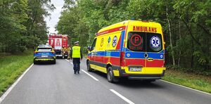 Miejsce zdarzenia drogowego, radiowóz, wóz strażacki, karetka pogotowia, strażacy i policjanci pracują na miejscu zdarzenia.