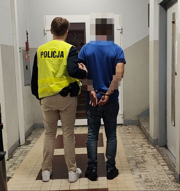 Policjant prowadzi zatrzymanego po korytarzu w budynku jednostki Policji.