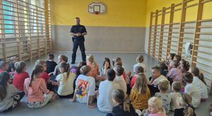 W sali gimnastycznej policjant prowadzi pogankę z dziećmi.