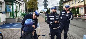 Policjanci z ruchu drogowego stoją na chodniku , jeden z policjantów zakłada  kask ochronny chłopcu na głowę.