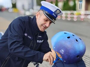 Policjant zakłada chłopcu kask ochronny na głowę.