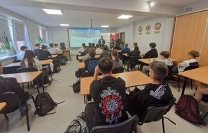 Dyrektor, policjant i przedstawiciel banku w sali lekcyjnej w trakcie spotkania z młodzieżą.