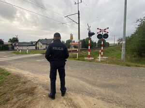 Policjant stoi przt przejeździe kolejowym.