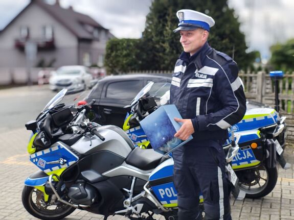 Policjant stoi przy motocyklu, trzyma w ręku pudełko z kaskiem.