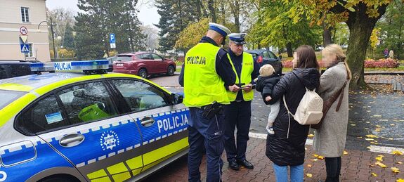 Radiowóz, obok stoją  policjanci rozmawiają z przechodniami.