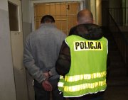 kolorowe zdjęcie ukazujące policjanta w odblaskowej kamizelce z napisem Policja prowadzącego zatrzymanego do kradzieży