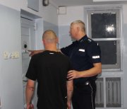 kolorowe zdjęcie ukazujące policjanta prowadzącego zatrzymanego do pomieszczeń dla osób zatrzymanych