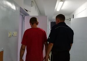 kolorowe zdjęcie przedstawiające zatrzymanego osadzanego przez policjanta w policyjnym areszcie